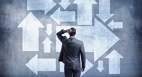 Business person in front of wall with arrows pointing in every direction.